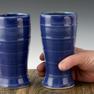 May include: Two tall, blue ceramic drinking glasses with a flared base and a striped design.