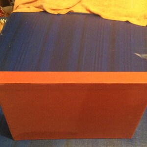 May include: A red, rectangular box with a smooth, flat surface. The box is closed and appears to be made of cardboard.