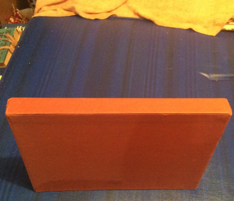 May include: A red, rectangular box with a smooth, flat surface. The box is closed and appears to be made of cardboard.