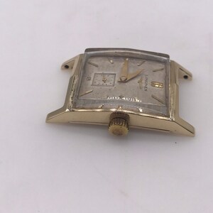May include: A vintage gold-toned Longines wristwatch with a rectangular face. The watch features a small subdial and gold hands. The watch face has the Longines logo and the words "Waterproof" and "Swiss Made".