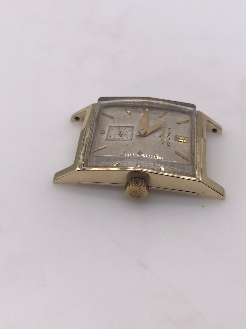 May include: A vintage gold-toned Longines wristwatch with a rectangular face. The watch features a small subdial and gold hands. The watch face has the Longines logo and the words "Waterproof" and "Swiss Made".