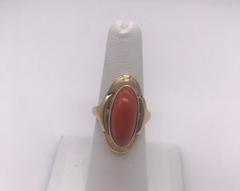 May include: A gold ring with an oval-shaped coral stone set in a delicate, ornate design.