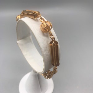 May include: A gold bracelet with a chain link design and round, textured ball accents. The bracelet has a clasp closure.