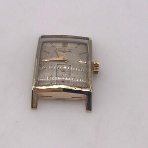 May include: A vintage rectangular Longines watch with a gold-tone case and a silver-tone face. The watch features gold hands and hour markers, and a small subdial. The Longines logo is visible at the top of the watch face.