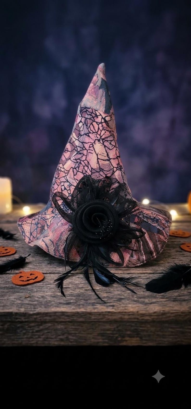 May include: A pointed hat featuring a pink and black cracked pattern fabric. The hat is adorned with a large black fabric rose and black feathers attached to the front. The design includes a wide brim and a tall, conical crown structure.