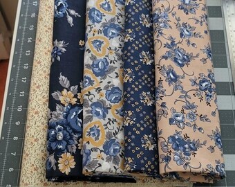 May include: A collection of five folded fabric pieces featuring floral patterns in shades of navy blue, mustard yellow, and beige, arranged on a cutting mat with sewing tools including two pairs of metal scissors, a seam ripper, and a pin cushion.