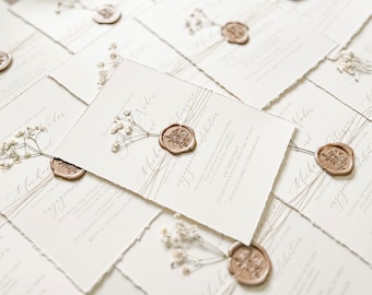 Op de afbeelding: Een stapel witte huwelijksuitnodigingen met een bruine waszegel en gedroogde bloemen. De uitnodigingen zijn in een handschrift en de tekst "verlovingsfeest" is zichtbaar.