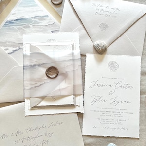 May include: Elegant wedding invitation suite featuring beach-themed stationery. Includes envelopes, invitation cards, and a translucent overlay with a seashell wax seal. The invitation text reads "Jessica Carter & Tyler Ingram".