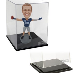 May include: A clear acrylic display case with a black base, showcasing a bobblehead figurine of a football player wearing a blue and white uniform with the number 88. The case is designed to protect and display collectibles.