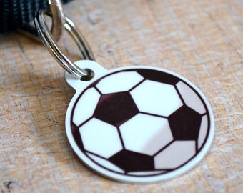 May include: A silver dog tag with a black and white soccer ball design.
