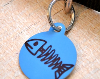May include: A blue round pet ID tag with a black fish bone design. The tag is attached to a silver ring.