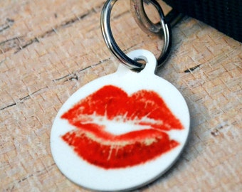 May include: White round dog tag with a red lip print. The tag is attached to a silver ring.