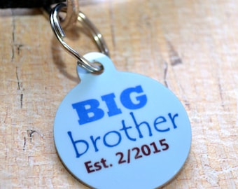 May include: Blue and white round dog tag with the text "BIG brother Est. 2/2015".