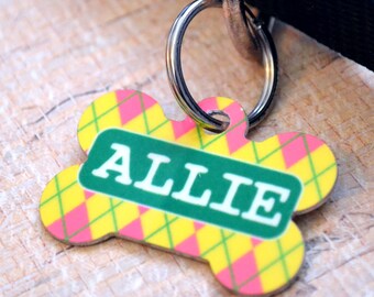 May include: A yellow, pink, and green bone-shaped dog tag with the name "Allie" printed in white on a green background.