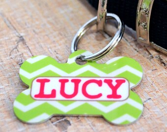May include: Green and white chevron dog tag with a bone shape and the name "LUCY" in pink letters.