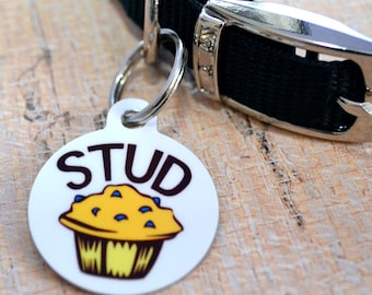 May include: White round dog tag with a blue and yellow muffin illustration and the word "STUD" in black letters.