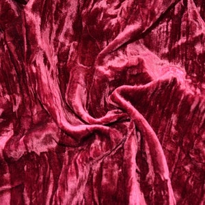 May include: Close-up of a deep red velvet fabric with a soft, plush texture. The fabric is draped and folded, creating a luxurious and elegant look.