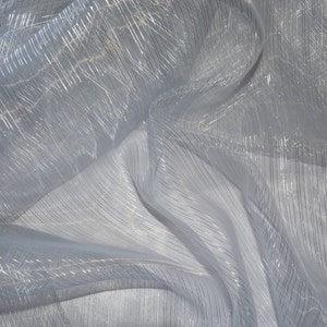 May include: A close-up of a sheer, white fabric with silver metallic stripes. The fabric is draped and folded, creating shadows and highlights. The stripes run both vertically and diagonally across the material, adding texture and visual interest.