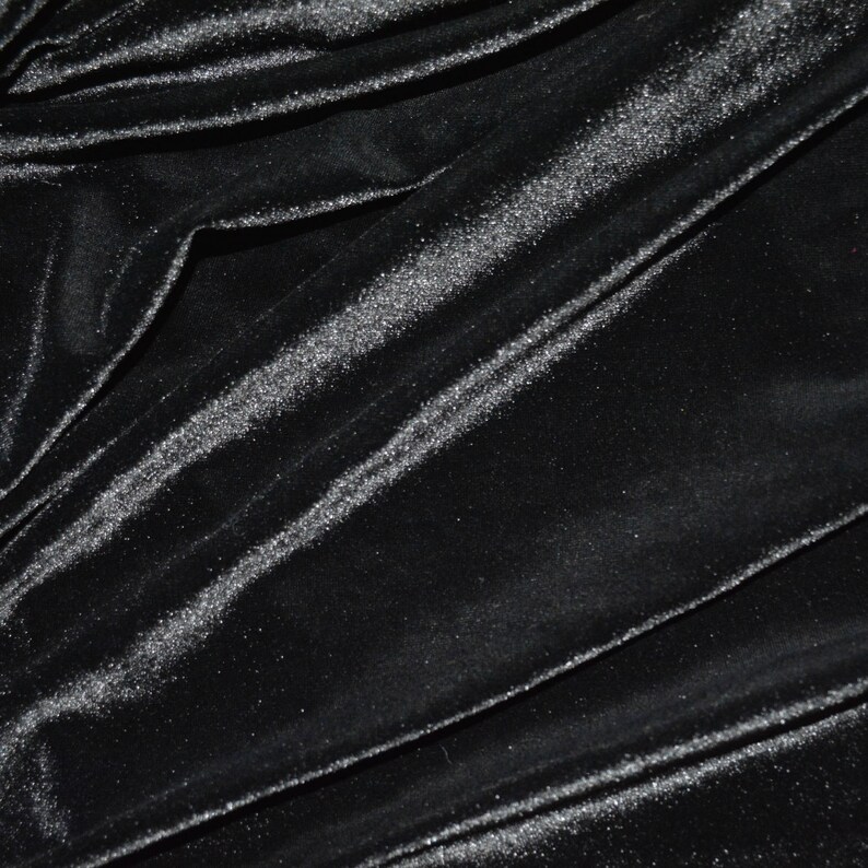 May include: Black velvet fabric with a subtle shimmer. The fabric is draped and folded, showing its texture and sheen.