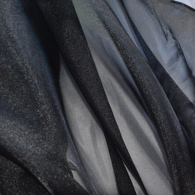 May include: Black sheer fabric with a subtle sparkle. The fabric is draped and folded, showing its texture and transparency.