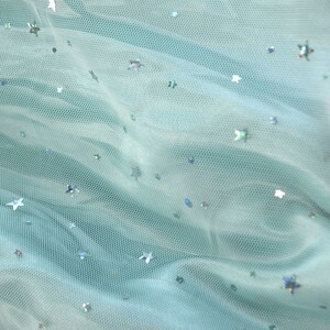 May include: A light blue tulle fabric with silver star-shaped sequins scattered across the surface.