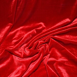 May include: Close-up of a vibrant red velvet fabric with a soft, lustrous texture. The fabric is draped and folded, creating shadows and highlights that emphasize its luxurious quality. The rich color and tactile appearance suggest a high-end textile.