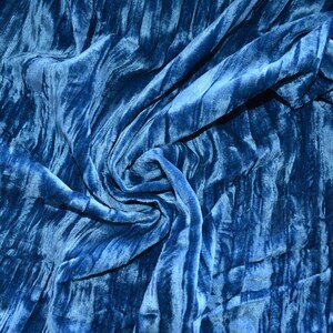 May include: A close-up of a blue velvet fabric with a soft, textured surface. The fabric is draped and folded, creating a swirling pattern.