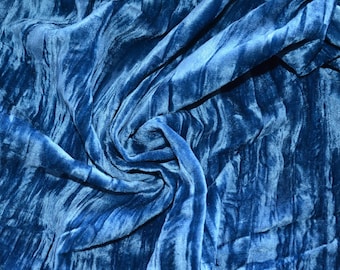 May include: A close-up of a blue velvet fabric with a soft, textured surface. The fabric is draped and folded, creating a swirling pattern.