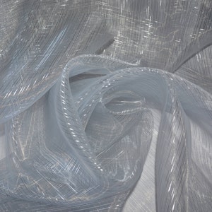 May include: A close-up of a light blue, sheer fabric with a subtle, shimmering effect. The fabric is draped and folded, creating soft curves and shadows. Thin, silver-colored lines run across the material, adding texture and visual interest.