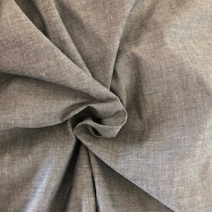May include: Close-up of a gray, textured fabric with a subtle sheen. The fabric is folded and draped, showcasing its soft and drapey texture.