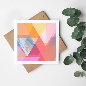 May include: A greeting card with an abstract geometric design featuring overlapping triangles in shades of pink, orange, yellow, and blue.
