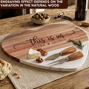 May include: A heart-shaped serving board made of natural wood and white marble. The wood section is engraved with the text "this is us" and "MARK ♥ QUINCY". Two cheese knives with wooden handles are placed on the marble section of the board.