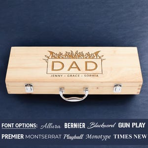 May include: Wooden box with a hinged lid and a metal handle. The box is engraved with the word "DAD" in a flame design. The names "Jenny, Grace, Sophia" are engraved below the word "DAD". The text "FONT OPTIONS: Allura BERNIER Blackword GUN PLAY PREMIER MONTSERRAT Playball Monotype TIMES NEW" is displayed below the box.