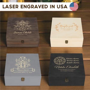 May include: Four wooden boxes with laser-engraved designs. The boxes are in various colours: dark brown, light beige, grey, and black. Each box has a hinged lid and a metal clasp. Text includes names, dates, and religious phrases. The text "LASER ENGRAVED IN USA" is at the top.