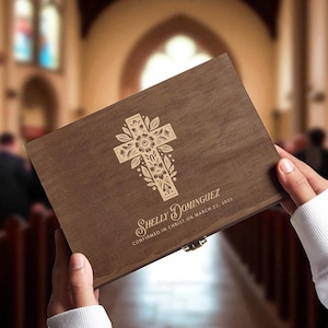 May include: A wooden box with a decorative cross design. The cross is adorned with floral elements. The box is engraved with the name "Shelly Dominguez" and the confirmation date "Confirmed in Christ on March 22, 2023."
