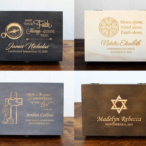 K&ouml;nnte beinhalten: Vier h&ouml;lzerne Andenkenboxen mit eingravierten Designs und Text. Die Boxen sind in verschiedenen Farben erh&auml;ltlich: Schwarz, helles Holz, Grau und Braun. Jede Box zeigt religi&ouml;se Symbole und personalisierte Namen mit Daten, geeignet f&uuml;r Firmungen, Erstkommunionen und andere religi&ouml;se Anl&auml;sse.