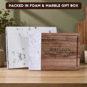 Custom laser engraved walnut and marble cutting board with family name, packed in a premium foam-lined marble gift box. Personalized charcuterie board gift for weddings, anniversaries, housewarmings, and Christmas.