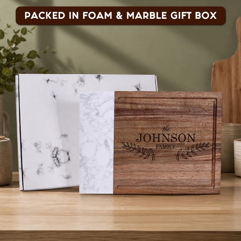 Custom laser engraved walnut and marble cutting board with family name, packed in a premium foam-lined marble gift box. Personalized charcuterie board gift for weddings, anniversaries, housewarmings, and Christmas.