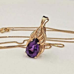 May include: A gold pendant necklace featuring a pear-shaped purple amethyst gemstone set in a decorative gold frame with three small clear accent stones at the top, suspended from a delicate gold box chain with a spring ring clasp closure.