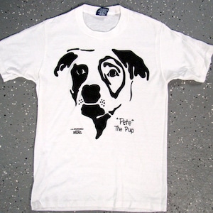 May include: White t-shirt featuring a black and white silhouette of a dog's head. The text "Pete" The Pup" is printed below the dog's head.