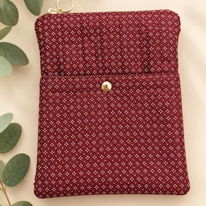 May include: A quilted burgundy pouch featuring a white geometric dot pattern. The rectangular pouch includes a top zipper closure with a gold-toned ring pull and a front pocket secured by a single gold-toned metal snap button fastener.