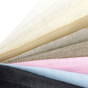 Pode incluir: Amostras de tecido de linho dispostas em leque, apresentando tons de branco, bege, cinza, rosa e azul. A textura tecida do tecido é visível, destacando as diferentes cores e texturas do material.