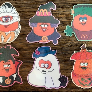 May include: Set of ten Halloween-themed stickers featuring various characters, including a witch, a mummy, a vampire, a ghost, and a pumpkin. Each sticker features a red and orange character with a white background.