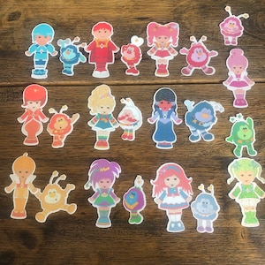 May include: A collection of 20 colorful cartoon character stickers. The characters are all wearing different outfits and have different hairstyles. Some of the characters are holding objects, such as a star, a flower, or a heart. The stickers are perfect for adding a touch of whimsy to any project.