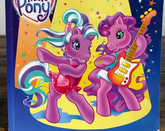 May include: A children's book titled "My Little Pony Pony Pop Stars". The cover features two purple cartoon ponies on a stage with a yellow background. One pony is dancing, and the other is playing a guitar.