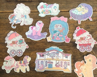May include: A set of ten colorful stickers featuring My Little Pony characters and scenes. The stickers are printed on a white background and feature pastel colors, including pink, blue, and yellow. The stickers depict a variety of scenes, including a pony rocking a horse, a pony in a carriage, and a pony in a house.