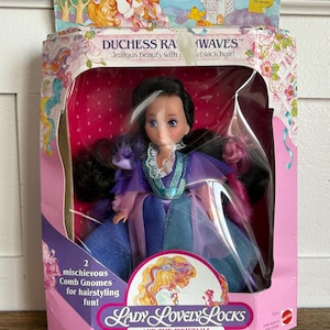 May include: A boxed Lady LovelyLocks Duchess Ravenwaves doll. The doll has black hair with a white streak and wears a blue and purple dress. The box features the text "A fairy tale world of Pixietail magic!" and "Lady LovelyLocks and the Pixietails."