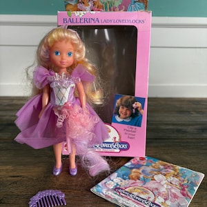 Könnte beinhalten: Eine Vintage Ballerina Lady Lovelylocks Puppe mit blondem Haar und einem lila Kleid. Die Puppe befindet sich in ihrer originalen rosa Schachtel, mit einem Kamm und einem Heft. Auf der Schachtel steht "Clip a Pixietail in your hair!"