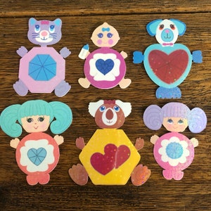 May include: Set of seven felt character appliques with a heart design. The characters include a koala, a baby, a cat, a dog, and three girls. The appliques are in various colors, including pink, blue, yellow, and green.