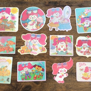 May include: A set of ten colorful stickers featuring a cartoon dog with pink hair and sunglasses. The stickers have different backgrounds and show the dog in various activities, such as eating, playing, and relaxing. The stickers are all labeled "Poochie".